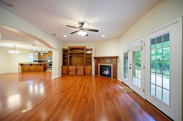 unfurnished living room featuring a glass covered fireplace, wood finished floors, decorative columns, a ceiling fan, and recessed lighting