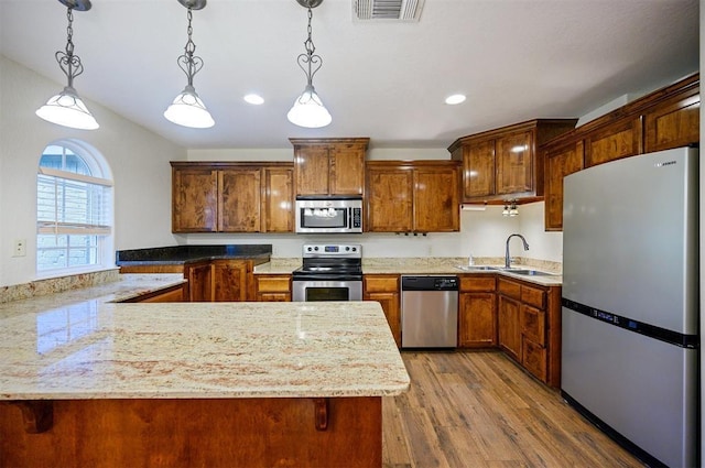 kitchen featuring stainless steel appliances, a sink, a peninsula, hanging light fixtures, and wood finished floors