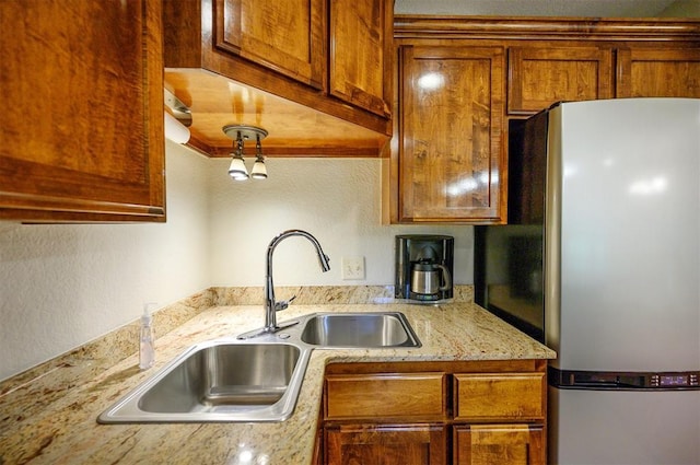 kitchen featuring freestanding refrigerator, a sink, brown cabinetry, and light stone counters