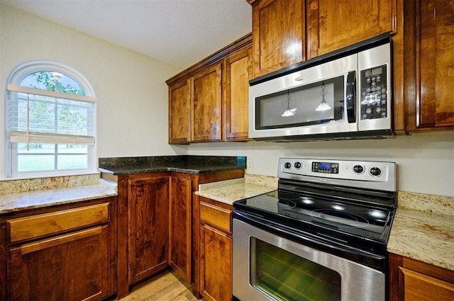 kitchen featuring stainless steel appliances, light stone counters, light wood finished floors, and brown cabinetry
