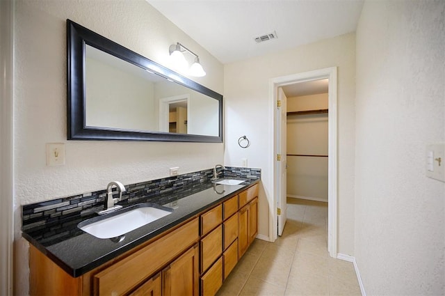 full bathroom with tile patterned floors, baseboards, double vanity, and a walk in closet