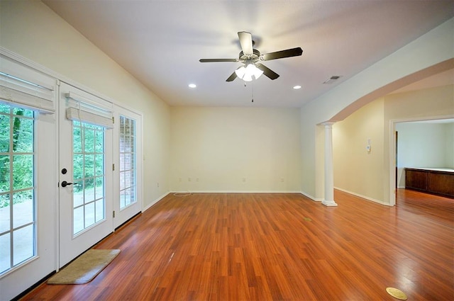 spare room with arched walkways, wood finished floors, decorative columns, a ceiling fan, and recessed lighting