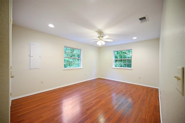 unfurnished room with a ceiling fan, plenty of natural light, electric panel, wood finished floors, and recessed lighting