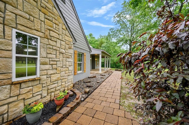 view of property exterior with stone siding and a patio area