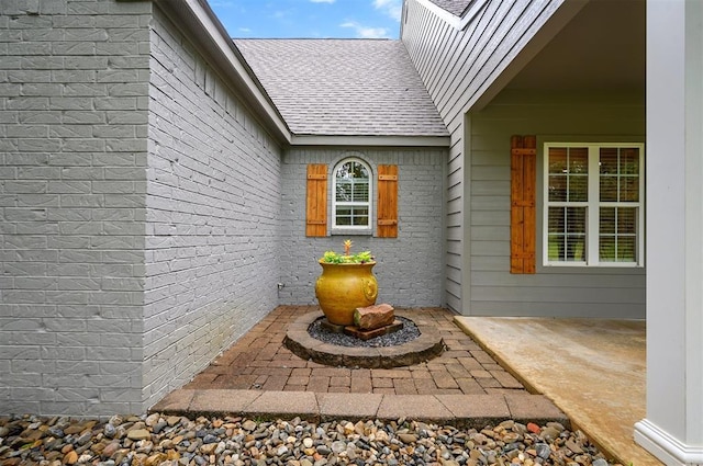 property entrance featuring brick siding, a patio, and roof with shingles