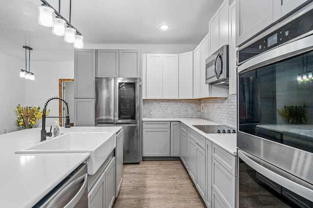 kitchen with stainless steel appliances, light countertops, tasteful backsplash, hanging light fixtures, and gray cabinetry