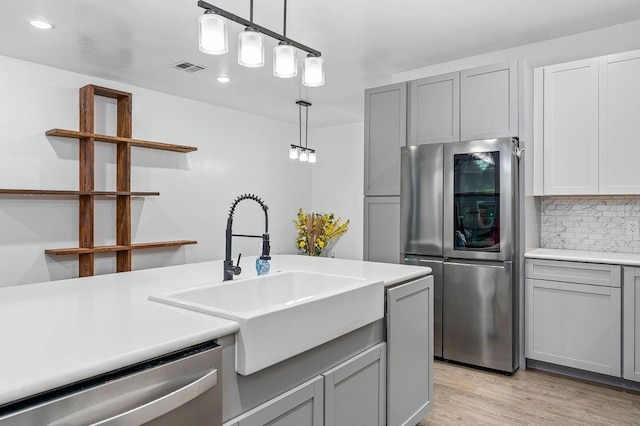 kitchen featuring stainless steel appliances, a sink, backsplash, open shelves, and gray cabinetry