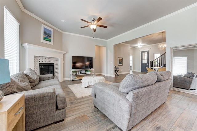 18337 Tombstone Trl, Norman, OK 73072 - living room with light wood-style floors, crown molding, a tiled fireplace, ceiling fan, and stairway