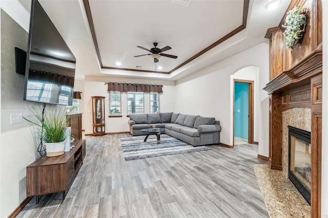 11423 Village Ave, Midwest City, OK 73130 - living area with a fireplace, a tray ceiling, baseboards, ceiling fan, and light wood-type flooring