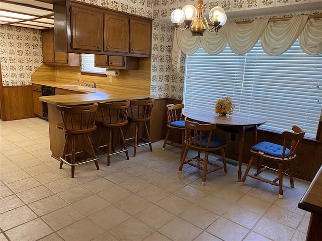 kitchen featuring wallpapered walls, wainscoting, a sink, light countertops, and a chandelier
