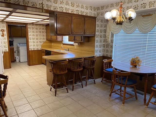 kitchen with wallpapered walls, washer / clothes dryer, wainscoting, a chandelier, and light countertops