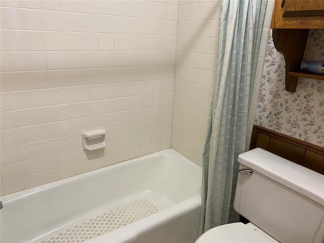 bathroom with wallpapered walls, toilet, shower / bath combination with curtain, and a wainscoted wall