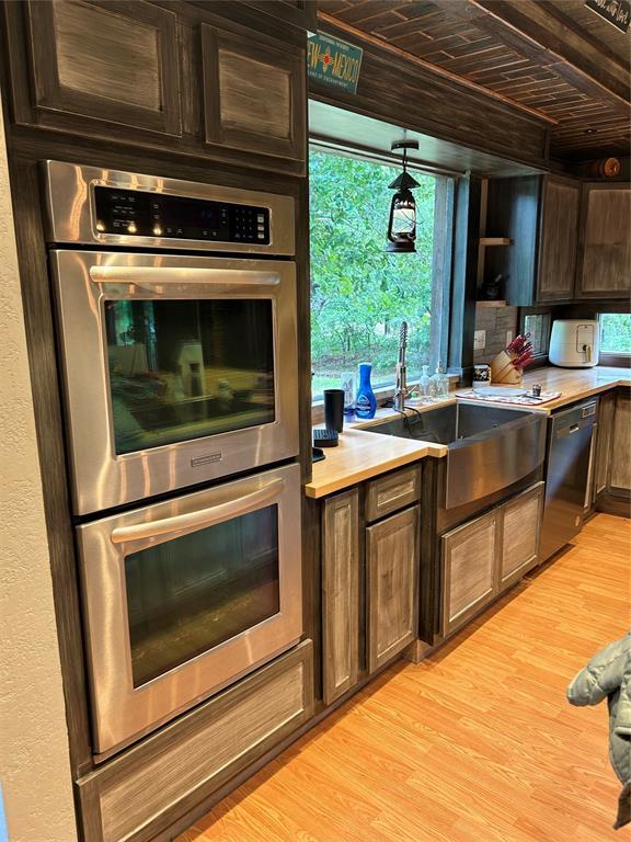 kitchen with stainless steel double oven, dishwasher, a sink, light countertops, and light wood-style floors