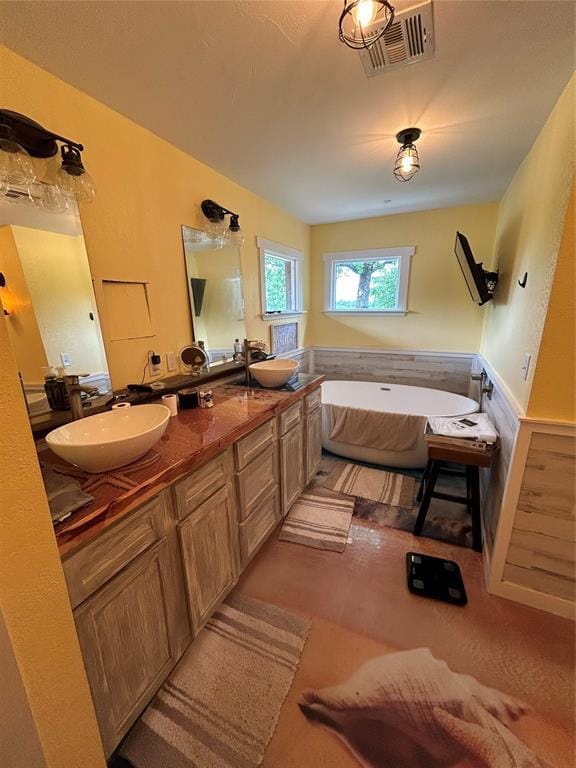full bathroom featuring a soaking tub, double vanity, and wainscoting