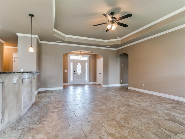 unfurnished living room with a raised ceiling, a ceiling fan, arched walkways, ornamental molding, and baseboards