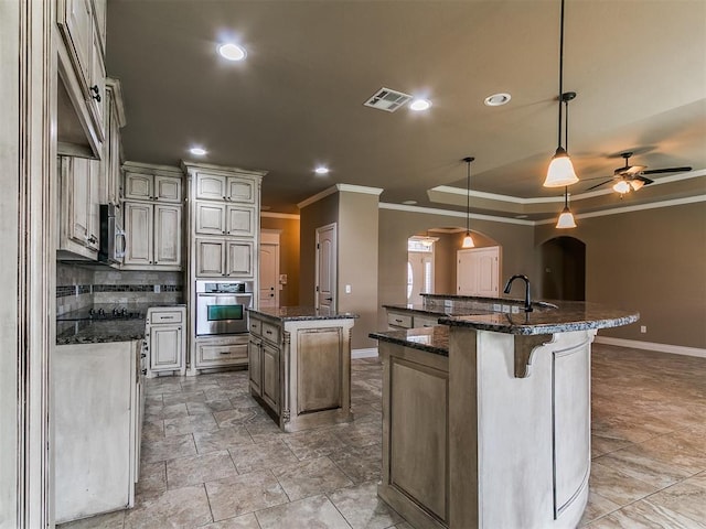 kitchen featuring arched walkways, a center island with sink, stainless steel appliances, crown molding, and baseboards