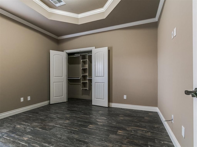 unfurnished bedroom featuring a tray ceiling, crown molding, wood finished floors, baseboards, and a closet