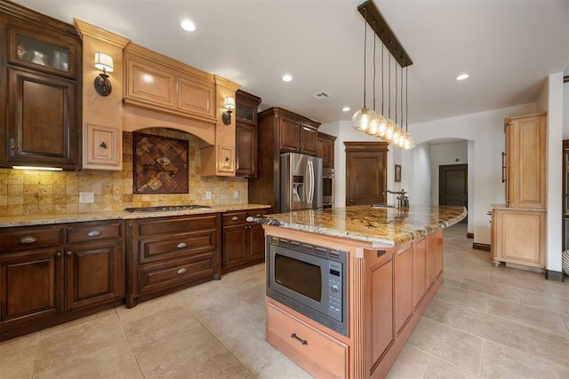 1401 Canyon Bridge Ln, Edmond, OK 73034 - kitchen with appliances with stainless steel finishes, tasteful backsplash, arched walkways, light stone counters, and a kitchen island with sink