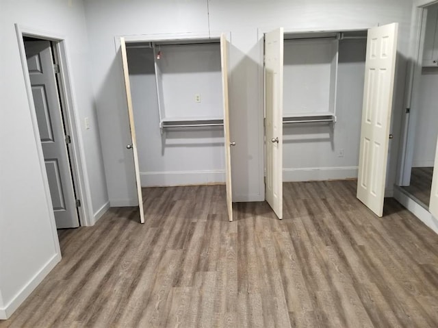 unfurnished bedroom with multiple closets, wood finished floors, and baseboards