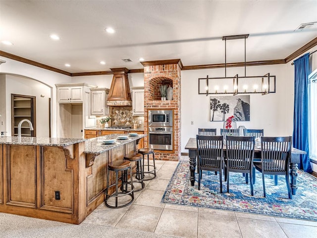 kitchen featuring appliances with stainless steel finishes, premium range hood, ornamental molding, light stone countertops, and decorative backsplash