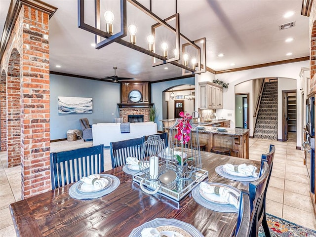 dining area featuring arched walkways, a brick fireplace, ornamental molding, a ceiling fan, and stairs