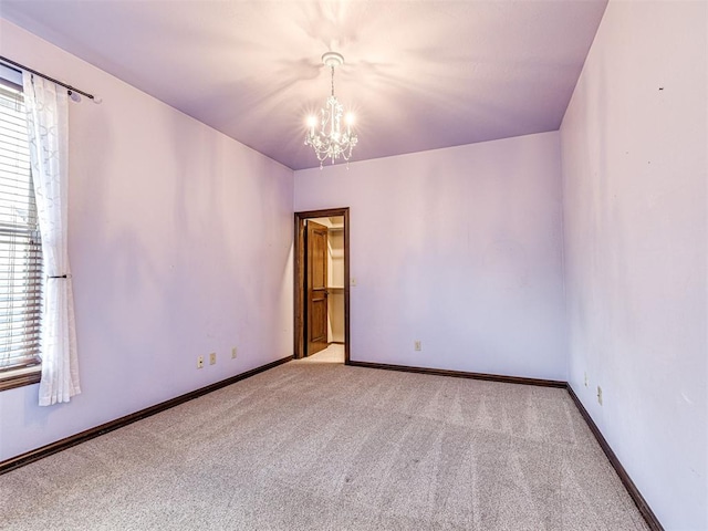 carpeted spare room featuring a chandelier, healthy amount of natural light, and baseboards