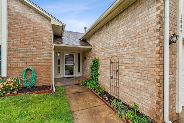 entrance to property featuring brick siding and roof with shingles