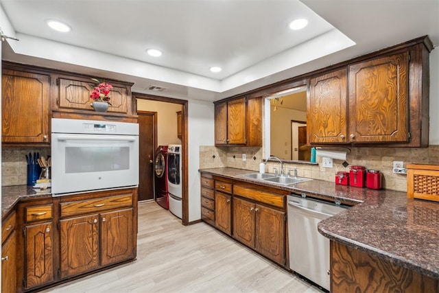 kitchen with white oven, stainless steel dishwasher, a sink, a raised ceiling, and washer and dryer