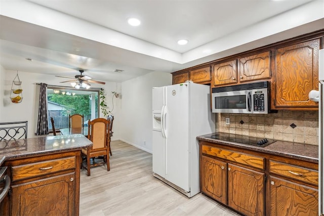 kitchen featuring stainless steel microwave, white refrigerator with ice dispenser, black electric cooktop, decorative backsplash, and light wood finished floors