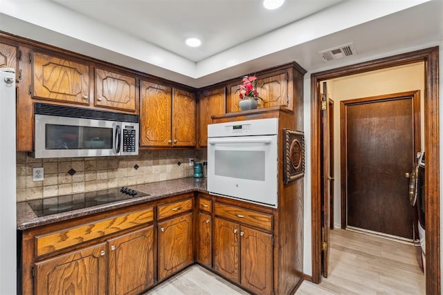 kitchen with stainless steel microwave, oven, black electric stovetop, brown cabinetry, and tasteful backsplash