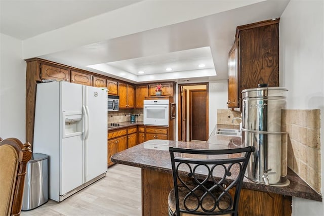 kitchen featuring white appliances, a raised ceiling, a peninsula, decorative backsplash, and a sink