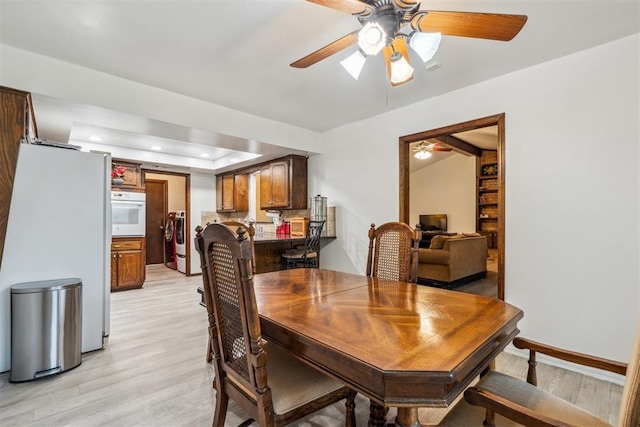 dining space with a ceiling fan, light wood-type flooring, recessed lighting, washer / dryer, and a raised ceiling