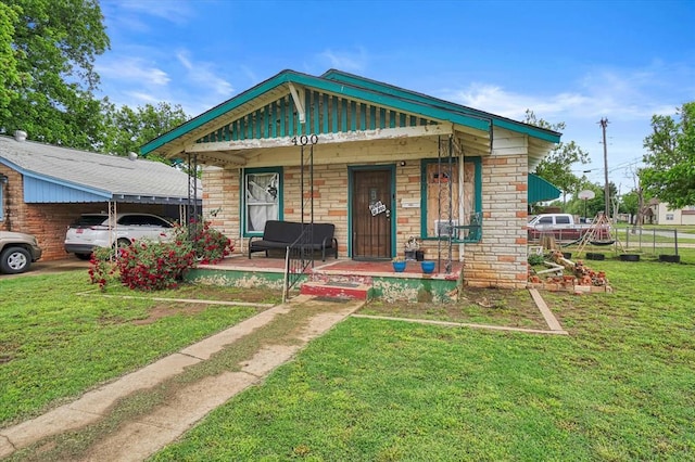view of front of property with covered porch, a front yard, stone siding, and a detached carport