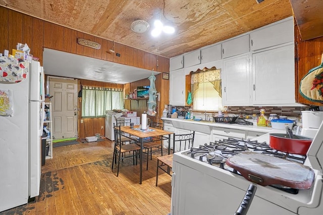 kitchen with white appliances, light wood-style flooring, healthy amount of natural light, wood walls, and light countertops