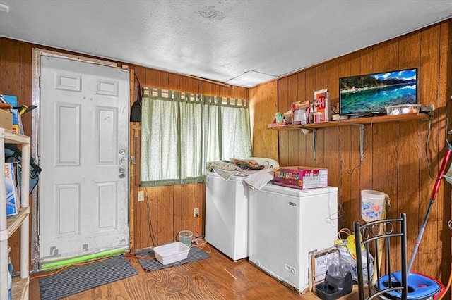 laundry room with wooden walls, washing machine and dryer, a textured ceiling, and wood finished floors
