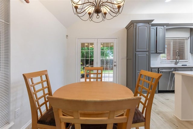 dining room featuring a chandelier, light wood finished floors, vaulted ceiling, and french doors
