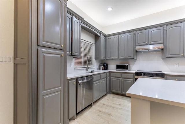 kitchen with appliances with stainless steel finishes, under cabinet range hood, a sink, gray cabinetry, and light countertops