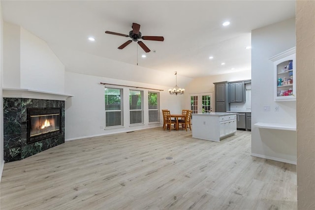 living area with vaulted ceiling, light wood-type flooring, a chandelier, a high end fireplace, and ceiling fan