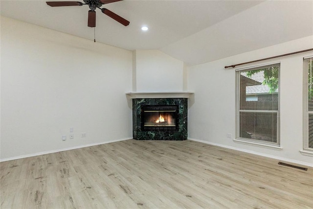 unfurnished living room with wood finished floors, a high end fireplace, vaulted ceiling, a ceiling fan, and baseboards