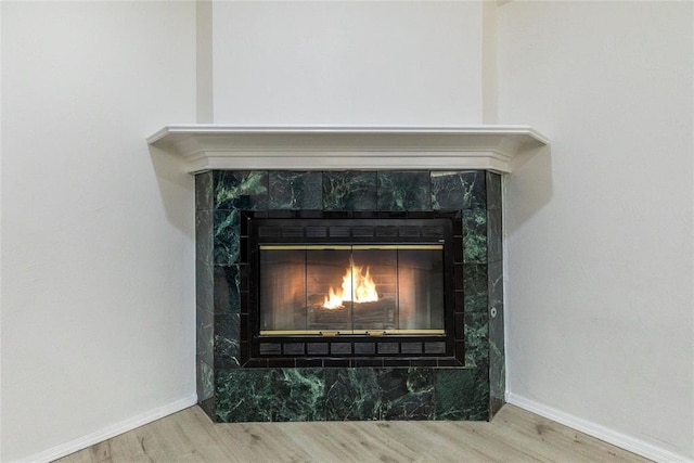 detailed view of a tile fireplace, wood finished floors, and baseboards