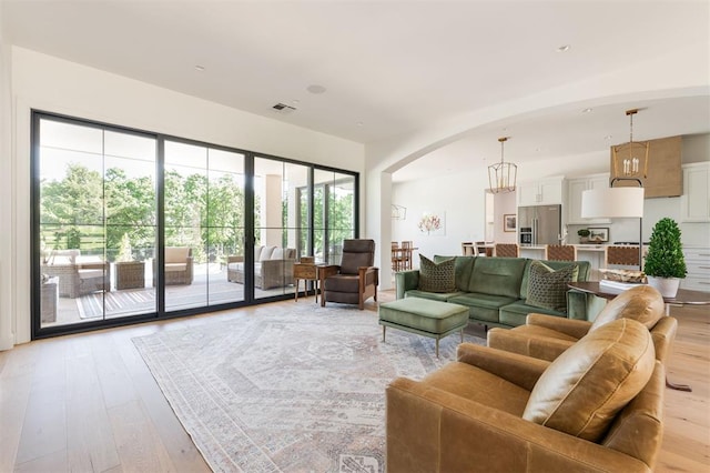 living area featuring light wood-style flooring, arched walkways, and a chandelier