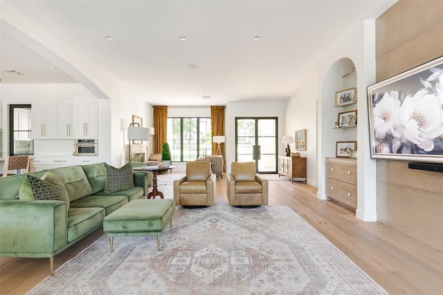 living area with light wood-style floors, arched walkways, and baseboards