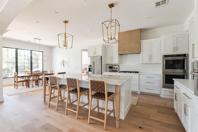 kitchen featuring appliances with stainless steel finishes, a chandelier, light wood-type flooring, a center island with sink, and a breakfast bar