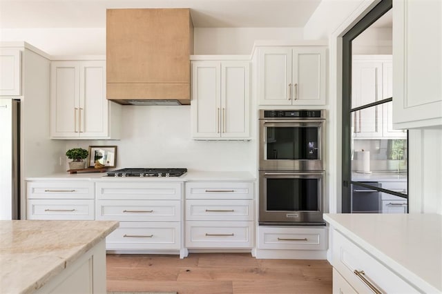 kitchen featuring stainless steel appliances, white cabinetry, light wood-style floors, and custom range hood