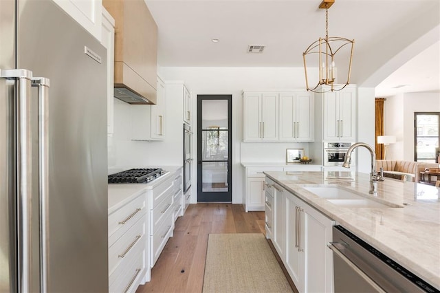 kitchen with stainless steel appliances, a sink, light wood finished floors, white cabinets, and light stone counters