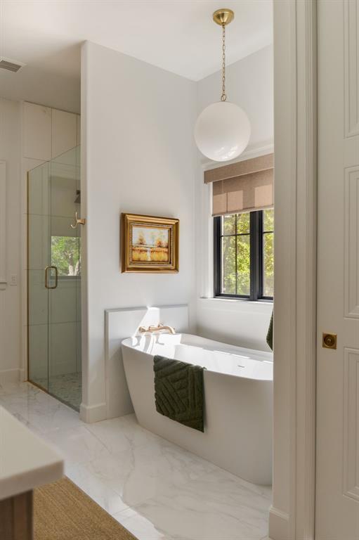 full bath with marble look tile flooring, a stall shower, and a freestanding tub