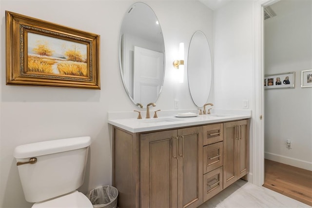 bathroom with toilet, double vanity, and baseboards
