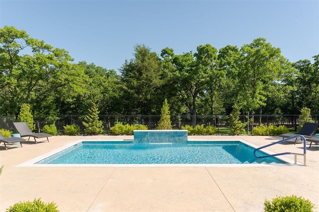 view of pool with fence, a patio, and view of wooded area