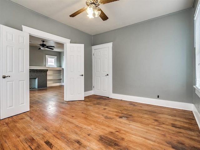 unfurnished bedroom featuring light wood-style flooring, baseboards, crown molding, a ceiling fan, and a brick fireplace