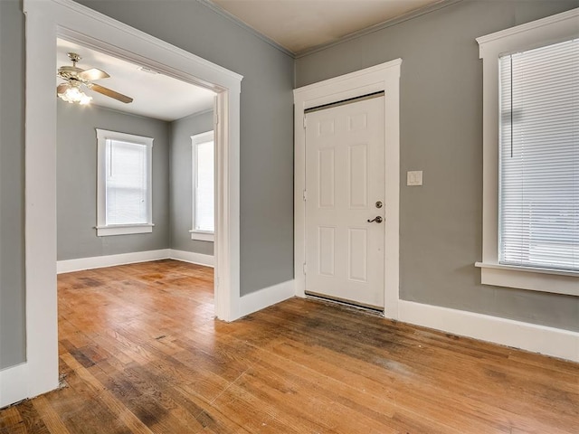 foyer entrance featuring wood finished floors, crown molding, baseboards, and a ceiling fan